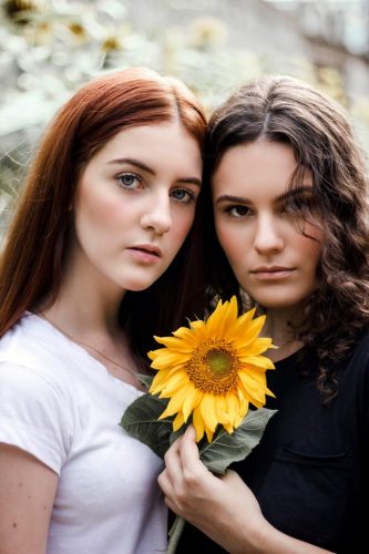 Bad parenting: Two women one wearing white with red hair and one wearing black with dark brown hair and a sunflower in the middle